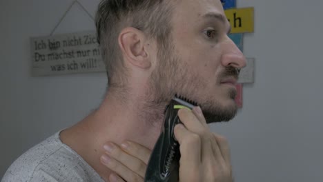 un hombre caucásico se está recortando el pelo facial con una afeitadora eléctrica para parecer suave, el primer plano muestra la cara de un hombre mientras se recorta y se afeita la barba