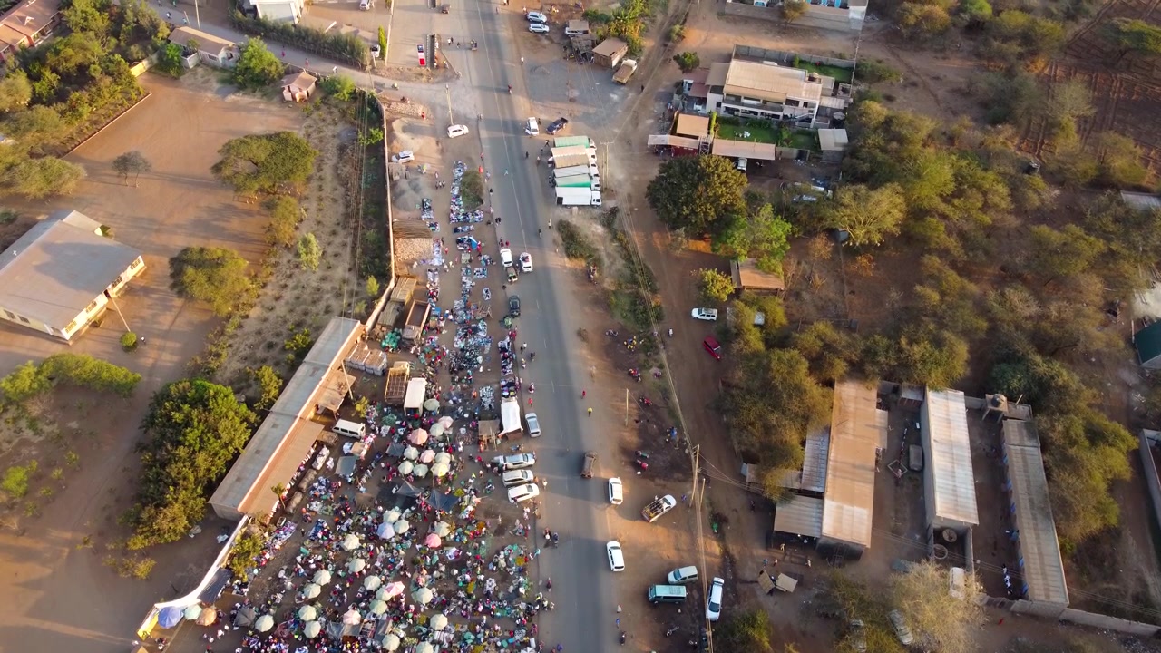 Splendida vista aerea di un mercato africano all'aperto con ombrelloni colorati, bancarelle affollate e gente del posto che commercia prodotti freschi sotto la calda luce del sole in Kenya.