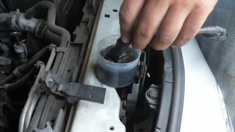 fingers dipping a cng or compressed natural gas injector of a car engine into a container with some cleaning liquid agent