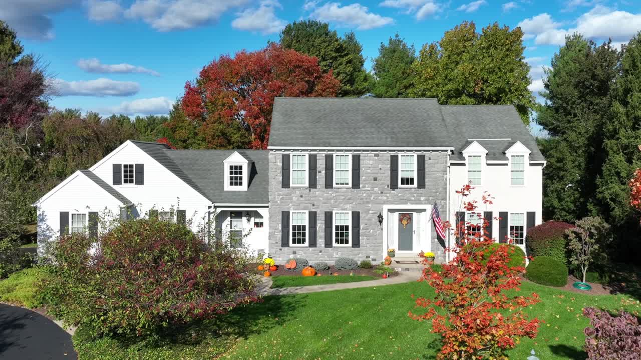 Suburban home in America with grey stone, white siding, colorful autumn trees, American flag, and Halloween decor