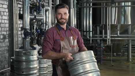 young male brewer in leather apron holds barrel with craft beer at modern brewery factory