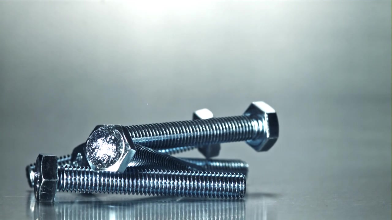 光沢のある金属製ボルトがスローモーションで落下し積み重なる様子