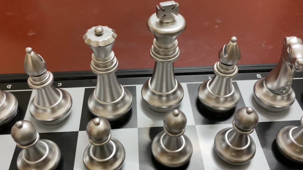 Indoor game: Silver colored chess pieces arranged on a board, ready to start game.