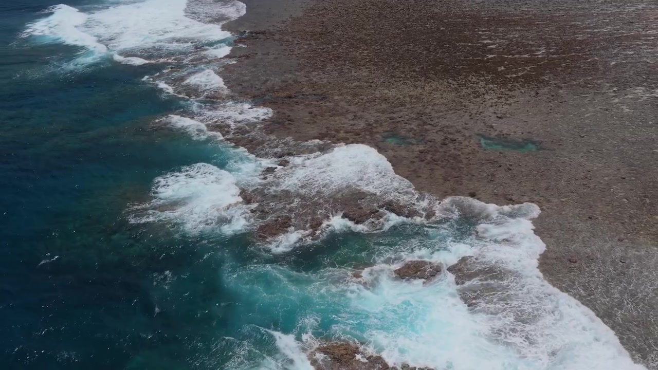 Inquadratura orizzontale ravvicinata con carrellata a destra, mentre il soggetto è rivolto a sinistra, sopra la barriera corallina rocciosa e le onde lungo la spiaggia di Waiwai