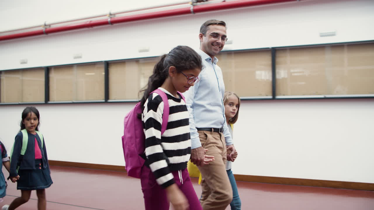 profesores masculinos y femeninos con un grupo de niños caminando en el pasillo de la escuela y yendo a clase