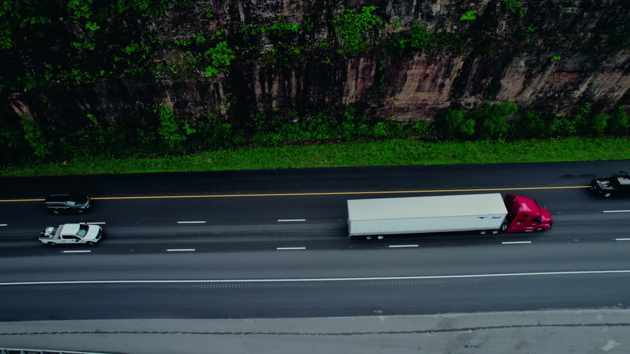 Red semi truck and SUV on cliffside interstate through Tennessee, showcasing scenic rock wall and freight travel.