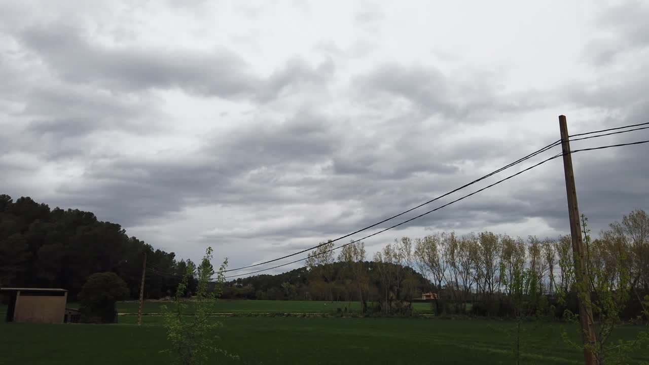 lapso de tiempo de un campo con postes eléctricos y árboles, día muy nublado, a punto de llover