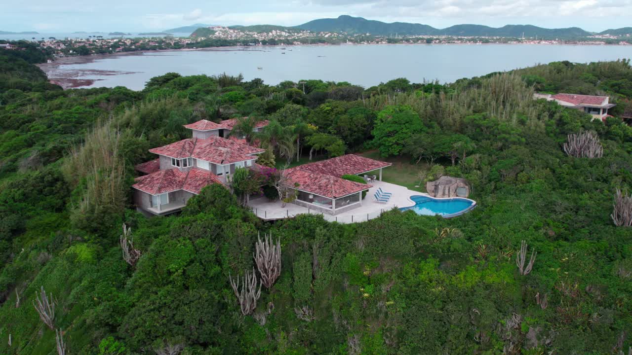 Aerial view revealing a lonely mansion with swimming pool on top of a dense mountain in B&uacute;zios, Brazil