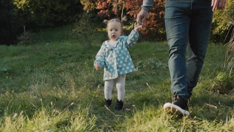 A-parent-leads-his-child-by-the-hand,-they-walk-together-in-the-park.