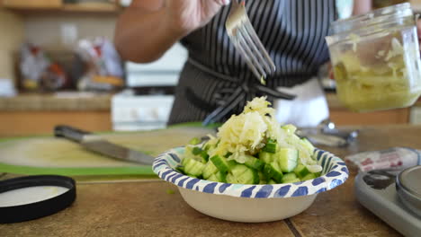 mixing sauerkraut with the cucumbers and other ingredients for a chopped salad - antipasto salad series