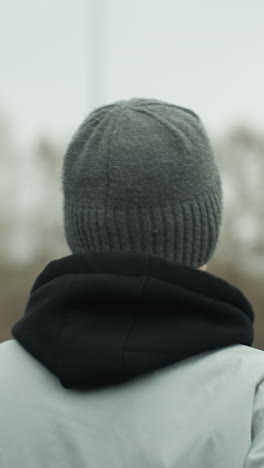 back view of a person jogging on a track, wearing a gray jacket and a black beanie, with a blurred view of a woman in a brown jacket and another person jogging opposite each other