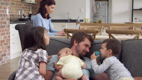 father plays with children as mother works on laptop