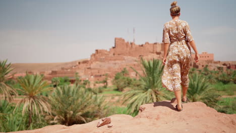 slo mo: mujer en vestido floral mira pueblo fortificado en marruecos