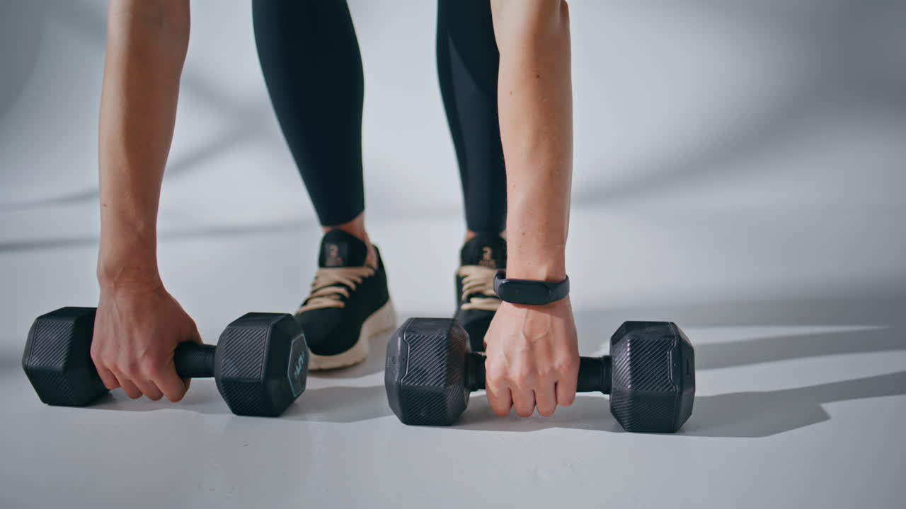 Unknown athlete taking dumbbells at white room closeup. Woman started workout