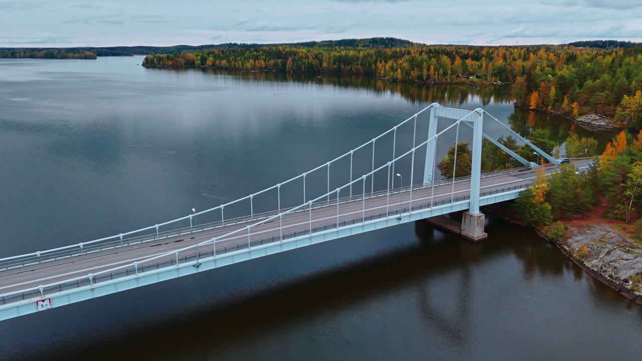Ripresa orbitante al rallentatore di un ponte sospeso che attraversa un fresco lago circondato da una foresta autunnale a Valkeakoski, Finlandia.