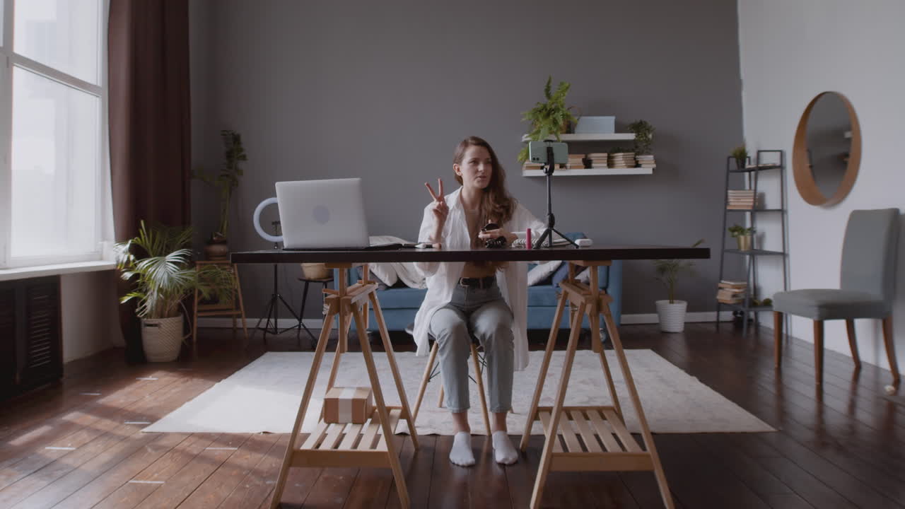스마트폰 카메라와 대화하고 메이크업 제품을 검토하는 아름다운 동영상 블로거 소녀의 넓은 사진