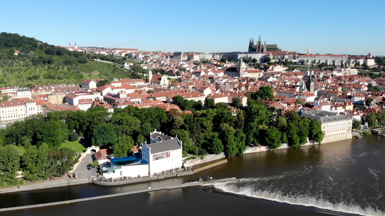 Sorvolo aereo lungo il fiume Moldava a Praga, Repubblica Ceca, con vista sul Castello di Praga, i tetti rossi di Malá Strana e il Ponte Carlo in una mattinata di sole.