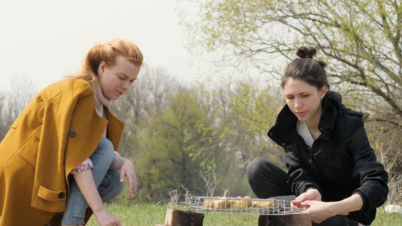 Two woman during cooking meat barbecue on fire at picnic on nature