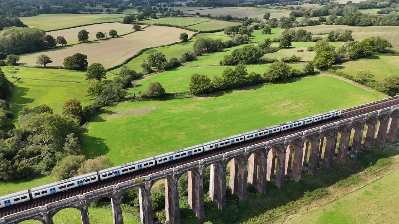 Scenic drone shot of Balcombe Viaduct in Sussex. Train travels smoothly over elegant Victorian arches, offering a mix of heritage engineering and natural English countryside