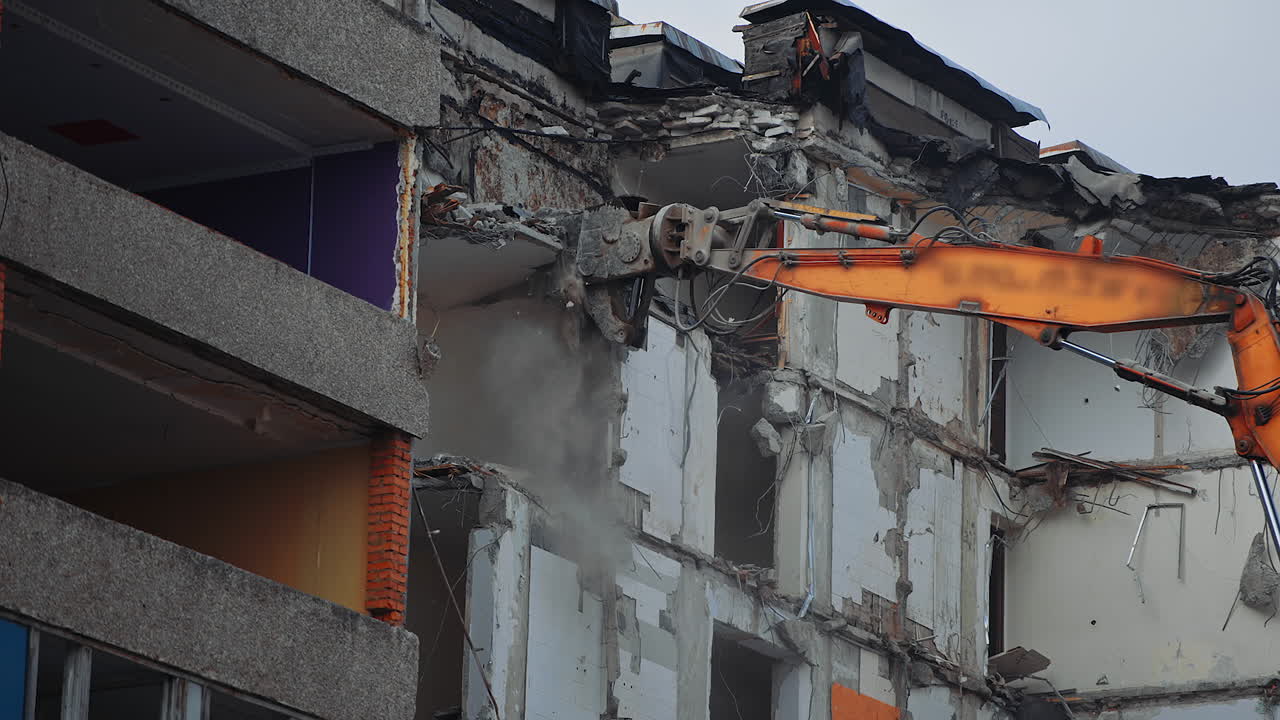 Hydraulic claw of excavator breaks easily the floors of an old building. Falling debris create thick dust cloud at the deconstruction site.