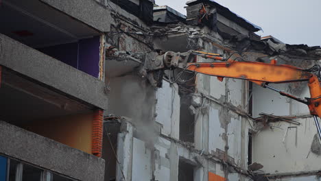 hydraulic claw of excavator breaks easily the floors of an old building. falling debris create thick dust cloud at the deconstruction site.