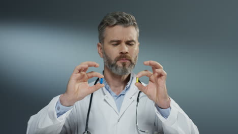 male physician holding two pills in hands, one yellow and one blue, while comparing them and studying carefully