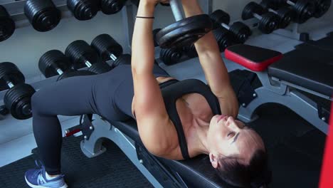 a beautiful woman lifts dumbbells lying on her back. professional athlete during muscle training in the gym. vertical video