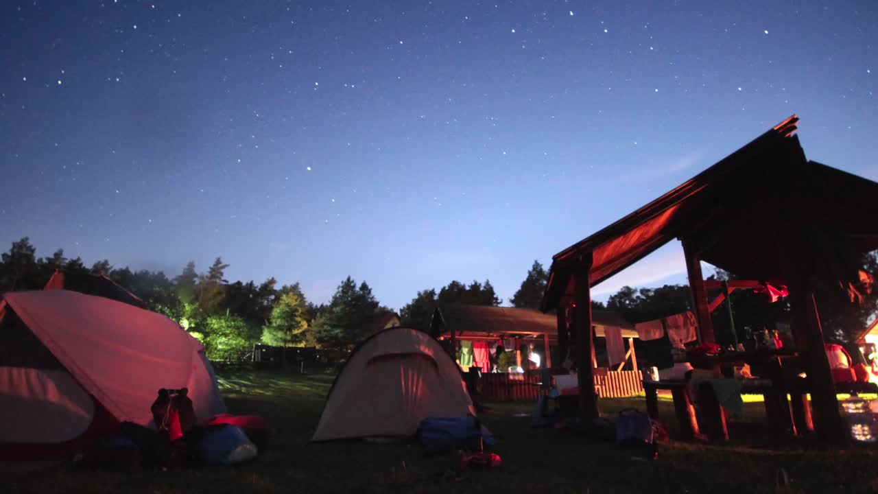 Time-lapse of the stars moving over a campsite with a lot of tents on it.