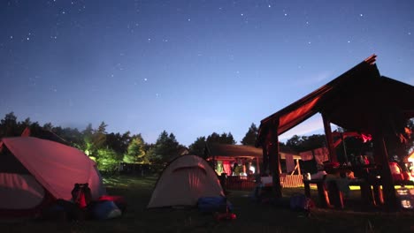 time-lapse of the stars moving over a campsite with a lot of tents on it.