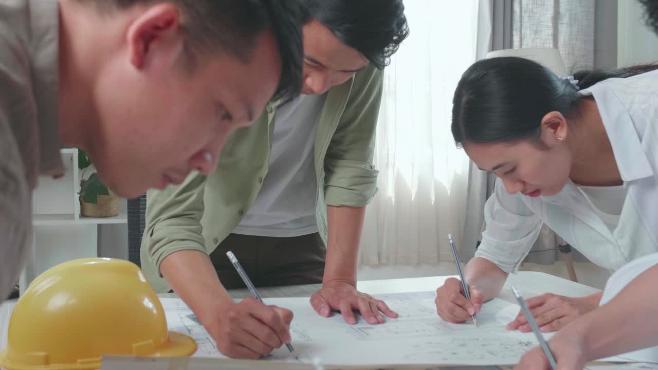 Group Of Asian Engineers Helping Each Other Drawing Building Construction At The Office