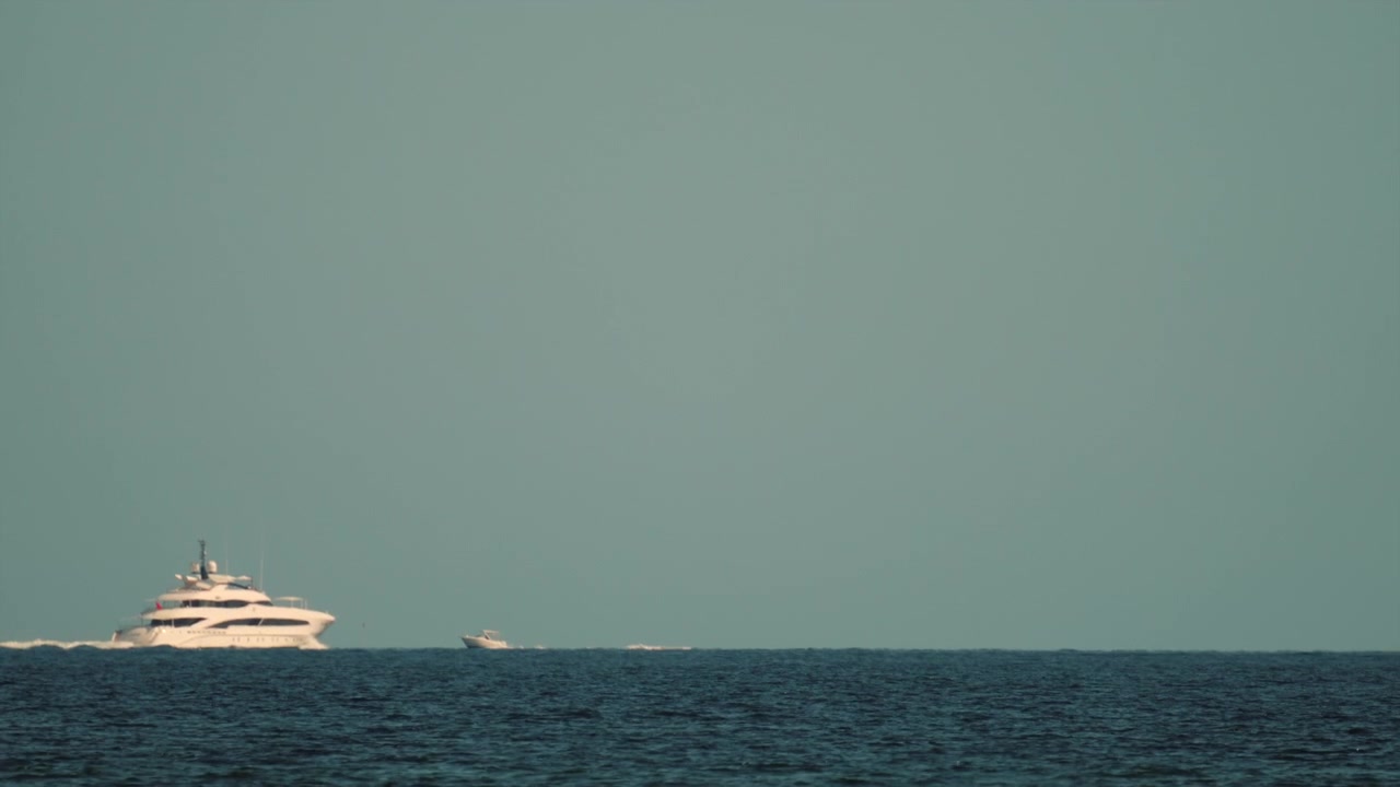 Yacht di lusso che naviga in acque profonde dell'oceano blu accanto a una barca più piccola, a simboleggiare ricchezza, viaggi e svago estivo.