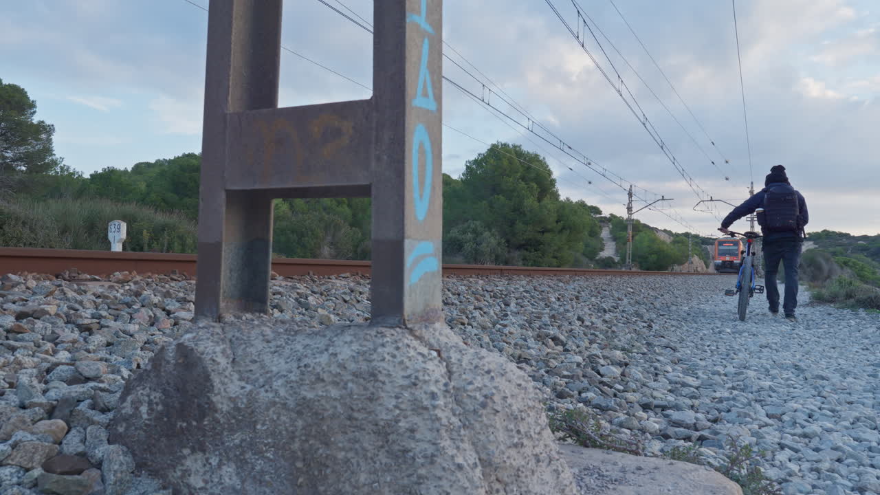 un hombre camina por las vías del tren mientras un tren de pasajeros pasa cerca, mientras el mar en calma baña el acantilado