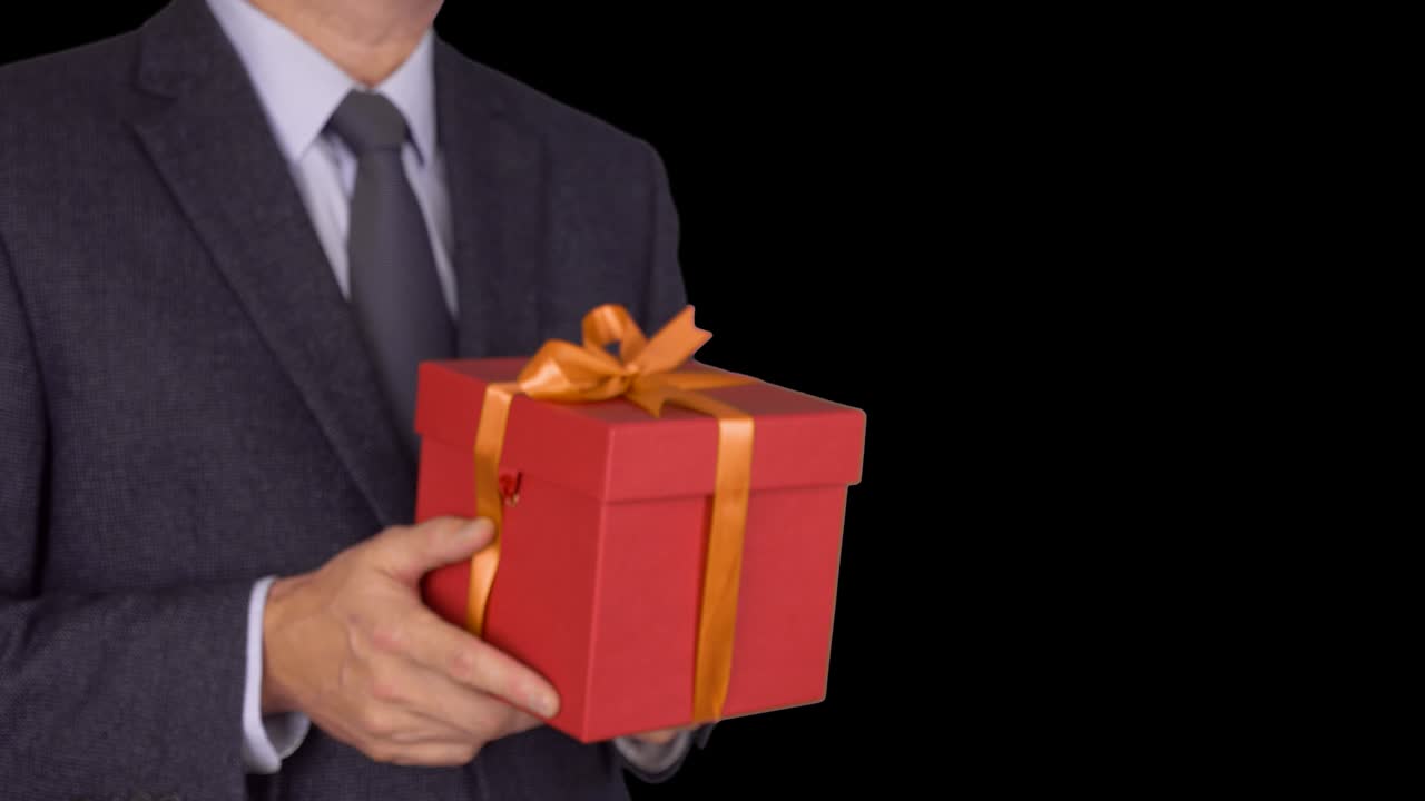 카우카스 사업가 들고 은 선물 상자를 주세요. 초점을 맞추지 않는 것에서 초점을 맞춘 움직임으로. 고전적인 비즈니스 슈트를 입은 성인 남자가 빨간 선물 상자 들고. 알파 채널 크로마 키 투명한 배경. 잠겼습니다.