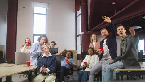 Grupo-De-Colegas-Multiétnicos-Viendo-Un-Partido-Deportivo,-Animando-Y-Apoyando-A-Su-Equipo-En-La-Oficina