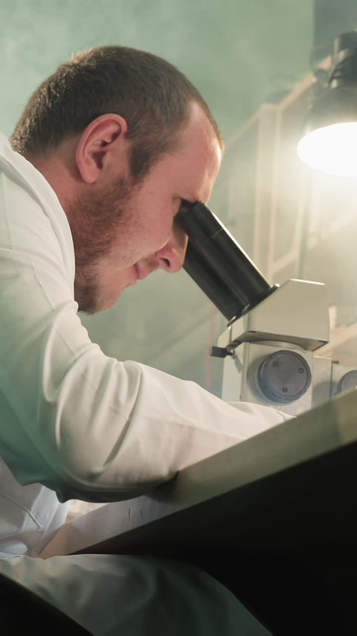 A close-up view of a technician in a lab coat meticulously working under a microscope, inspecting an electronic circuit board, with a desk lamp on been reflected on the screen
