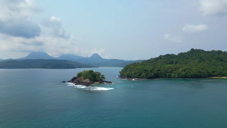 aerial tracking shot low in front of prince island coast and a small islet,ilha do principe,africa