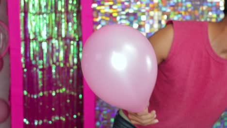 person in pink shirt inflating pink balloon against shiny sequin backdrop