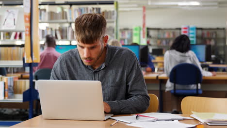 estudiante masculino trabajando en una computadora portátil en la biblioteca de la universidad