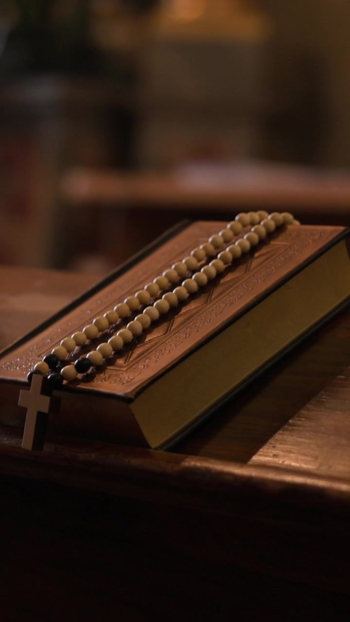 Catholic bible and rosary with cross resting on a wooden church pew symbolizing christian faith