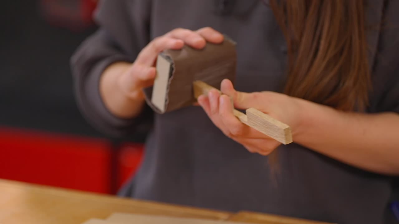 Video ravvicinato di mani che levigano un piccolo pezzo di legno con carta vetrata. Processo di finitura della lavorazione del legno, artigianato fatto a mano, creazione di mobili fai da te e dettaglio di levigatura della superficie