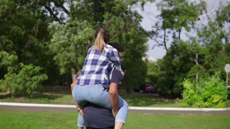 handsome african guy piggybacking his caucasian happy girlfriend and spinning around running on the green grass in the sunny