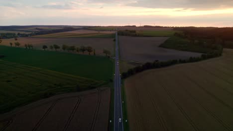 Long-and-straight-road-with-passing-cars-leading-uphill-to-the-golden-horizon-where-the-sun-sets