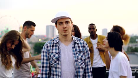 portrait of sad handsome man looking at camera at rooftop party then starting dancing, jumping and having fun. entertainment, modern city and people concept.