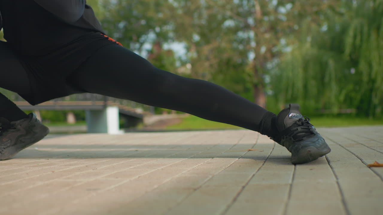 wide lateral lunge on boardwalk with trainer demonstrating controlled sidetoside mobility and strength female athlete in black leggings and rugged boots stretching inner thighs and stabilizing core