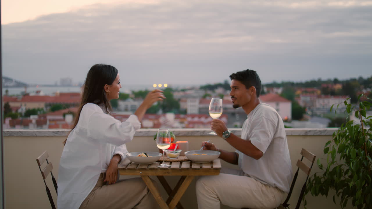 Coniugi felici che bevono champagne in terrazza, con zoom indietro. Un uomo premuroso si prende cura della moglie.