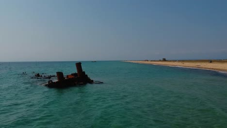 Panorámica-Reveladora-De-Una-Toma-Aérea-De-Un-Naufragio-Que-Se-Extiende-Hacia-El-Océano-Sobre-Una-Costa-De-Arena-Dorada-Y-El-Mar-Azul-Del-Mar-Mediterráneo-Cerca-De-Tesalónica,-Grecia-En-Epanomi