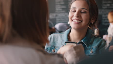 Hermosa-Mujer-Charlando-Con-Un-Amigo-En-Un-Café-Mostrando-Chismes-De-Redes-Sociales-De-Teléfonos-Inteligentes-Disfrutando-De-Una-Conversación-En-Un-Concurrido-Restaurante