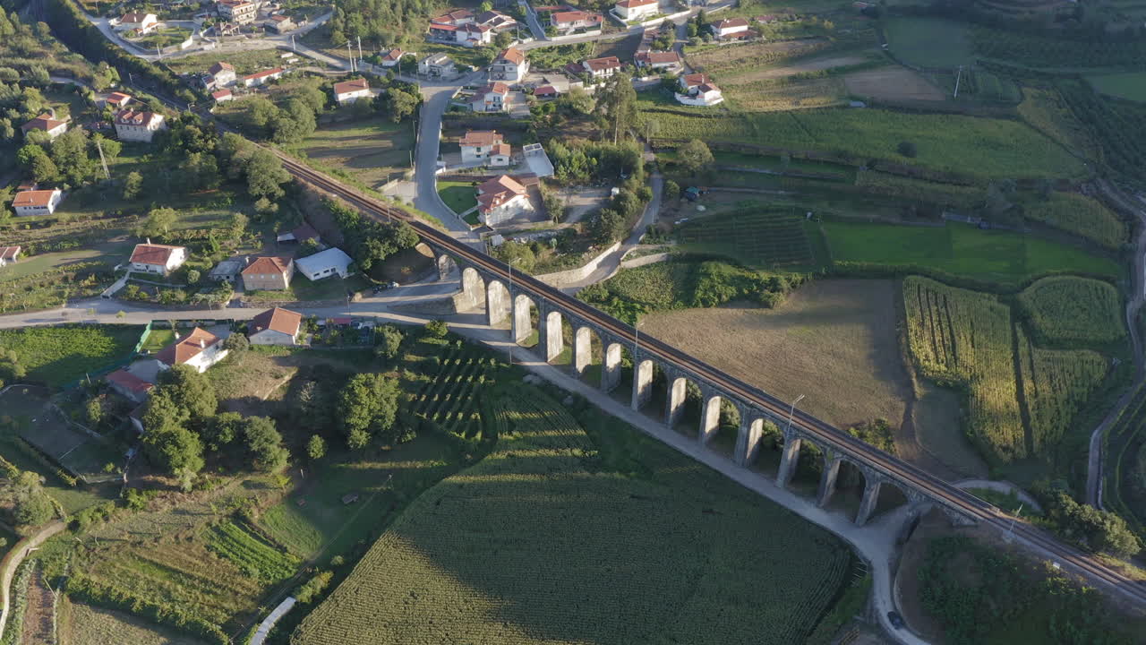 снимок с воздуха, кружащий вокруг старого арочного железнодорожного моста, окруженного полями, отбрасывающего тень на кукурузное поле - понте сека, дурраэс, барселос