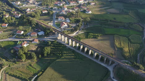 toma aérea dando vueltas alrededor del antiguo puente ferroviario de arco rodeado de campos de cultivo, proyectando sombra en el campo de maíz - ponte seca, durrães, barcelos