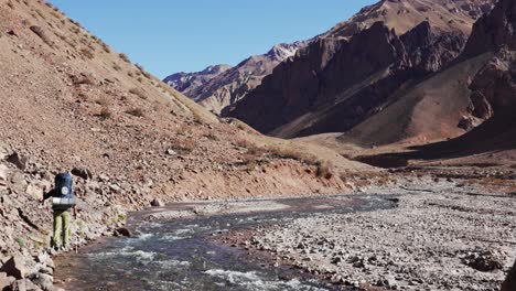 a hiker going up along the edge of a river in the andes mountains near aconcagua. mendoza, argentina.